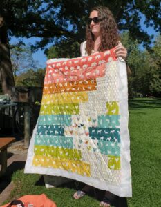 woman holding up multi color quilt